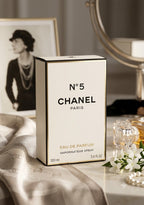 Chanel No 5 Eau de Parfum 100ml box displayed on a marble surface with a silk cloth, pearls, and a vintage-style mirror in the background.
